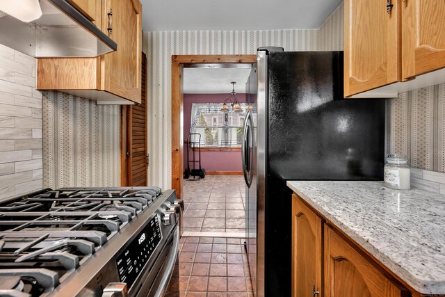 39 Smith St, Bristol, CT 06010 - kitchen featuring wallpapered walls, appliances with stainless steel finishes, under cabinet range hood, dark tile patterned flooring, and light stone counters