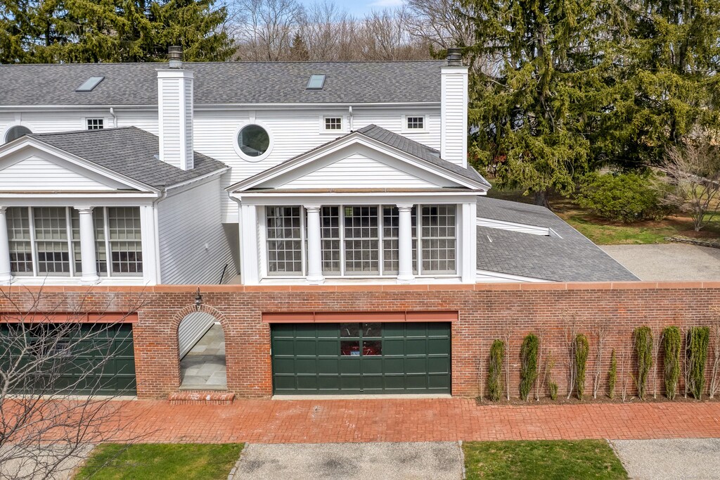 view of front facade featuring brick siding, driveway, a shingled roof, and a chimney