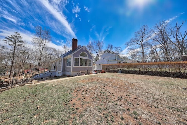 back of property featuring fence, a lawn, and a chimney