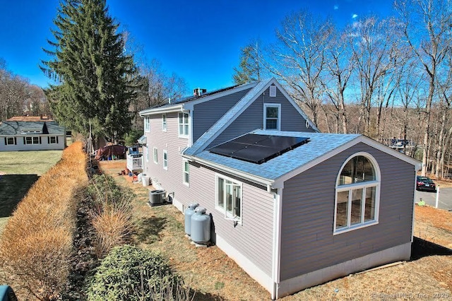 view of home's exterior with cooling unit and a shingled roof