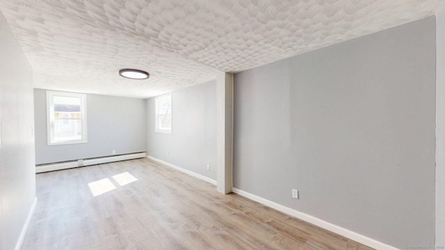 basement featuring a baseboard heating unit, wood finished floors, a textured ceiling, and baseboards