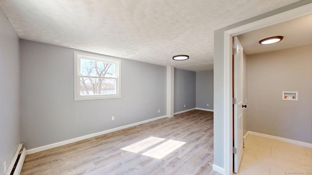 basement featuring baseboards, a textured ceiling, light wood finished floors, and baseboard heating