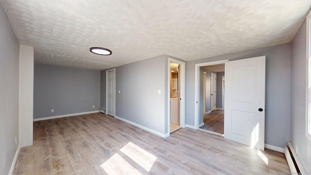 spare room with a baseboard radiator, baseboards, a textured ceiling, and light wood-style flooring
