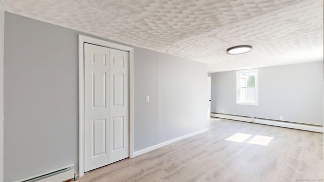 interior space with a baseboard heating unit, wood finished floors, a textured ceiling, and baseboards