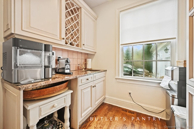 kitchen featuring light stone counters, wood finished floors, a sink, baseboards, and tasteful backsplash