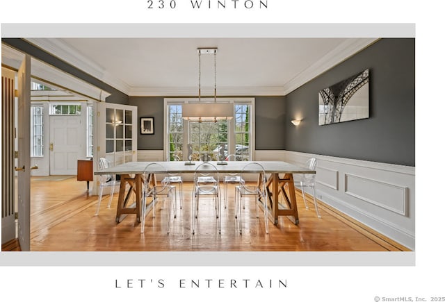 dining room featuring wainscoting, a decorative wall, ornamental molding, and wood finished floors