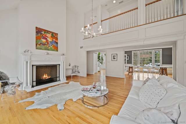 living area featuring a fireplace with flush hearth, wood finished floors, a towering ceiling, and a notable chandelier