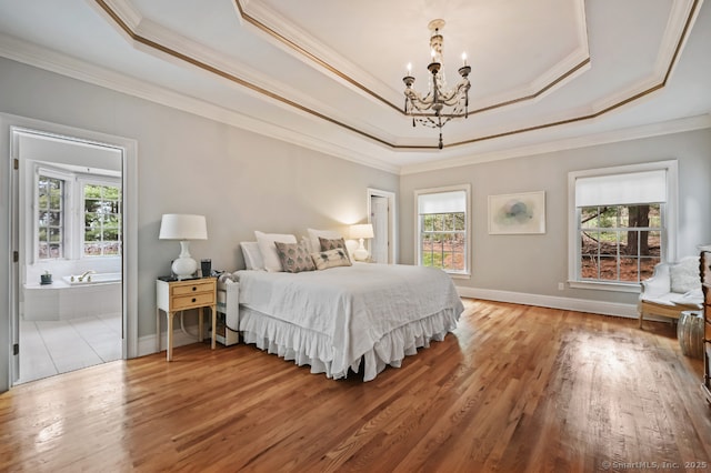 bedroom featuring an inviting chandelier, ornamental molding, wood finished floors, and a tray ceiling