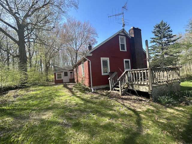 view of side of home with a deck, a yard, and a chimney