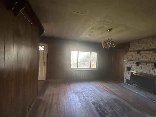 unfurnished living room with radiator heating unit, wood finished floors, an inviting chandelier, and a large fireplace