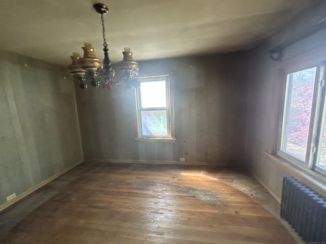 empty room featuring baseboards, radiator, a notable chandelier, and wood finished floors