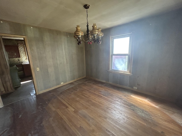 unfurnished dining area featuring baseboards, wood walls, wood finished floors, and an inviting chandelier