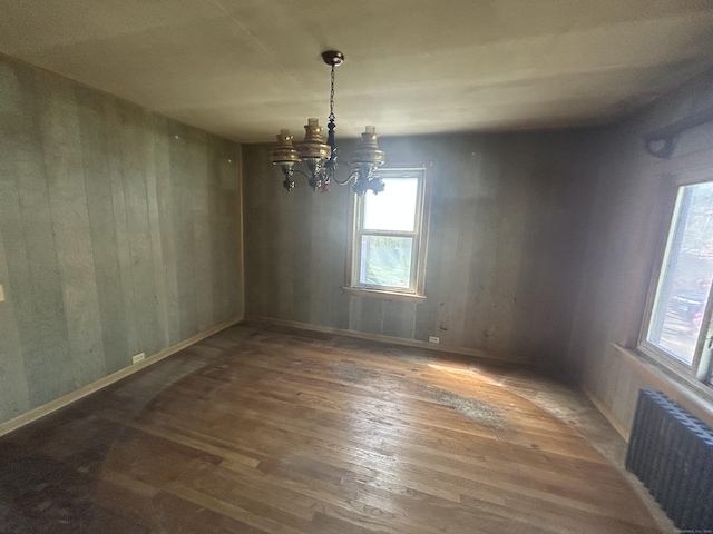 unfurnished dining area with an inviting chandelier, a wealth of natural light, hardwood / wood-style floors, and radiator