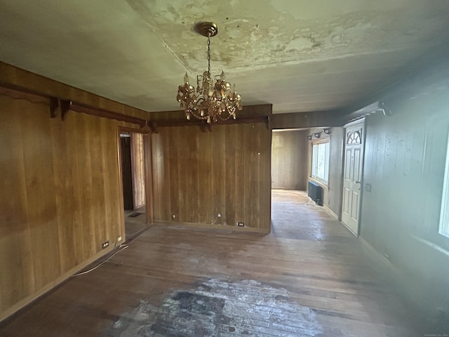 unfurnished dining area with wooden walls, a chandelier, and wood finished floors