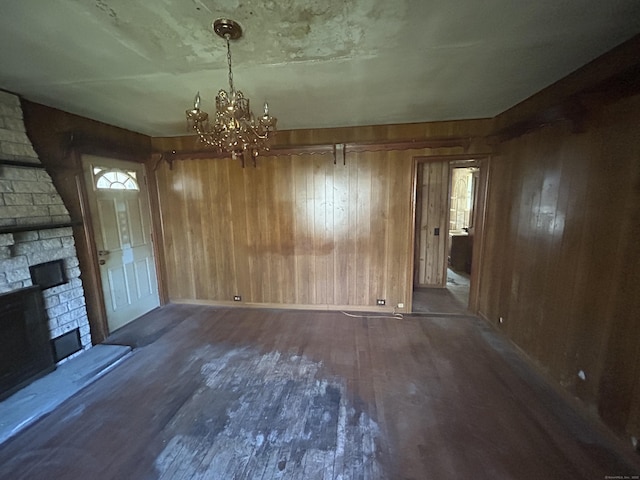 unfurnished dining area with wood walls, wood finished floors, a fireplace, and a notable chandelier