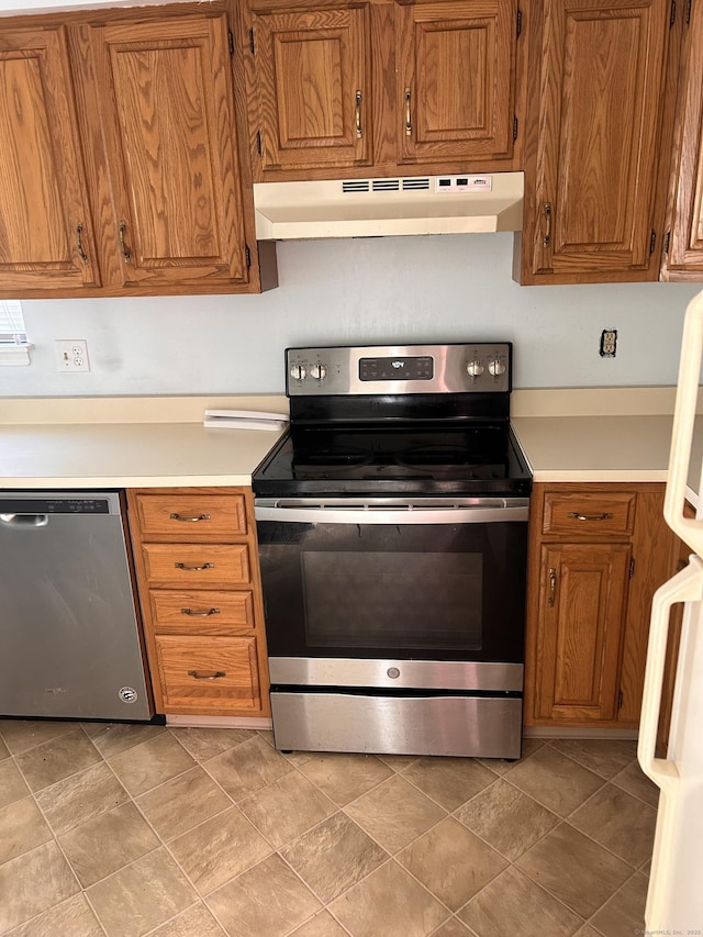kitchen featuring brown cabinetry, light countertops, under cabinet range hood, and stainless steel appliances