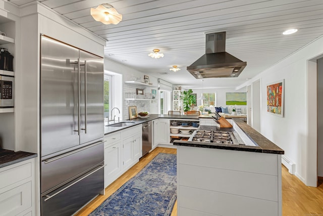 kitchen featuring open shelves, dark countertops, stainless steel appliances, plenty of natural light, and wall chimney range hood