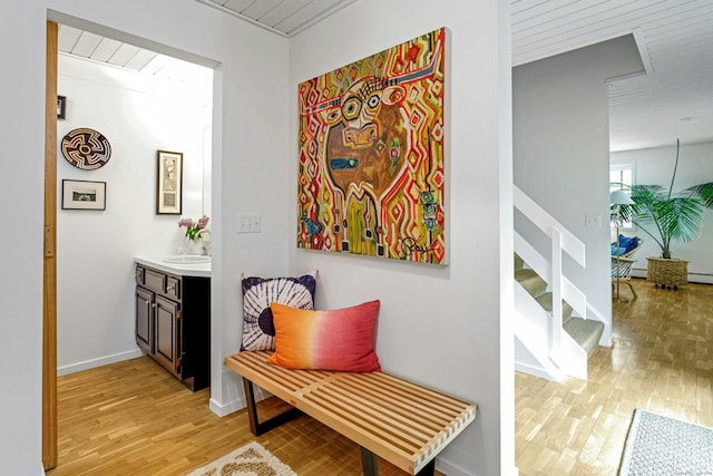 hall featuring light wood-type flooring, stairway, baseboards, and a sink