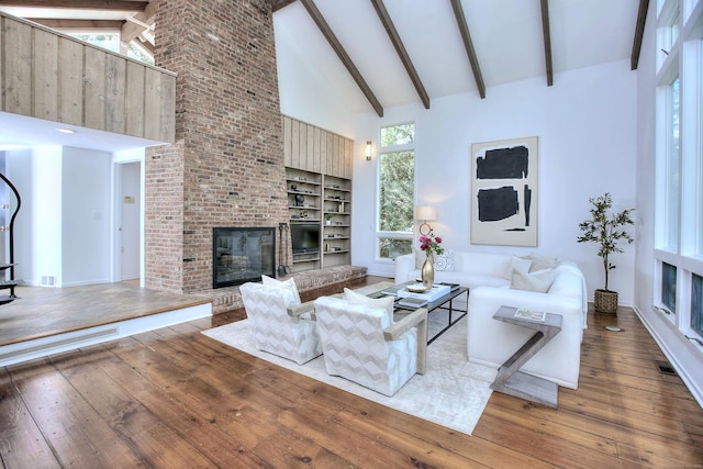 living room featuring hardwood / wood-style flooring, high vaulted ceiling, a brick fireplace, and beam ceiling