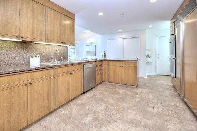 kitchen with appliances with stainless steel finishes, a sink, decorative backsplash, baseboards, and a peninsula