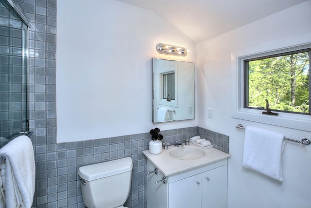 bathroom with lofted ceiling, vanity, toilet, tile walls, and a tile shower