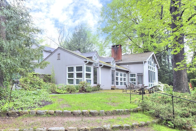 back of house featuring a chimney and a lawn