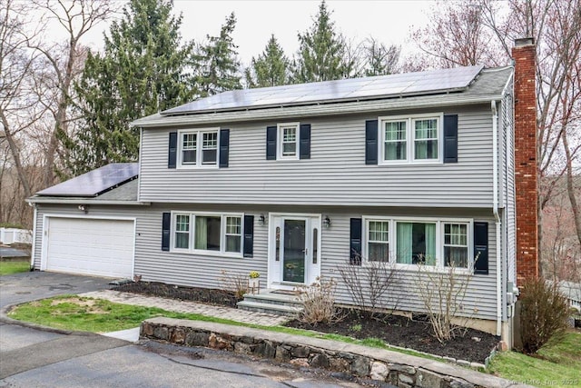 colonial-style house with a chimney, solar panels, driveway, and an attached garage