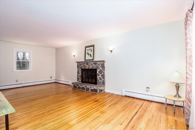 unfurnished living room with baseboard heating, wood-type flooring, baseboards, and a fireplace