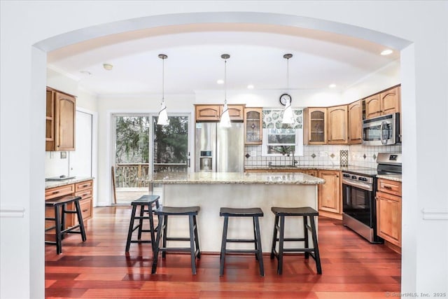 kitchen featuring ornamental molding, a breakfast bar area, appliances with stainless steel finishes, and glass insert cabinets