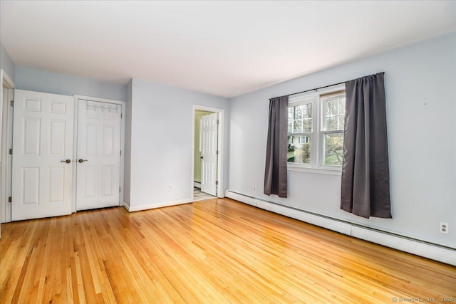 unfurnished bedroom featuring baseboards, a baseboard heating unit, light wood-style floors, and a closet
