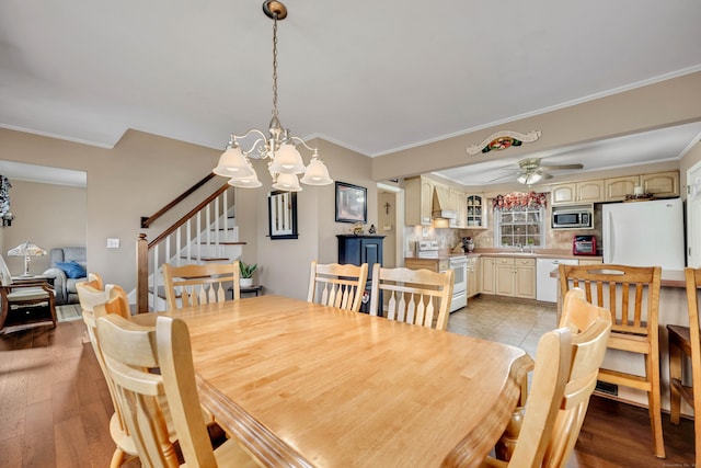 dining area featuring light wood-style floors, ornamental molding, ceiling fan with notable chandelier, and stairs