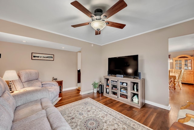 living area with ornamental molding, ceiling fan, wood finished floors, and baseboards