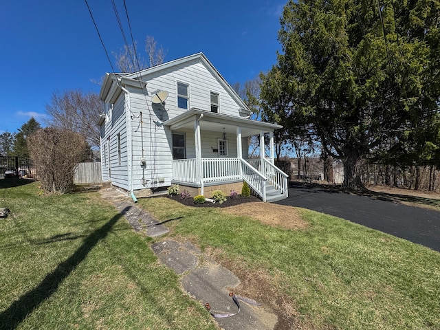 view of front facade with a front lawn, covered porch, and fence
