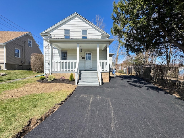 shotgun-style home featuring covered porch, a front yard, and driveway