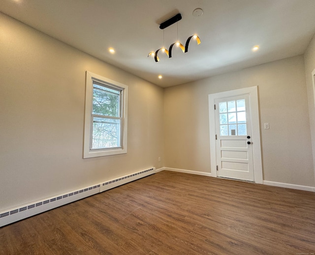 spare room featuring dark wood-style flooring, a baseboard radiator, and a healthy amount of sunlight