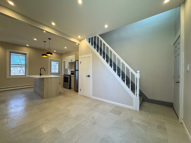 kitchen with freestanding refrigerator, stainless steel electric range oven, recessed lighting, a baseboard heating unit, and a center island with sink