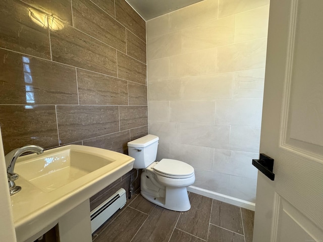 half bath featuring a baseboard heating unit, toilet, tile walls, a sink, and wood finished floors