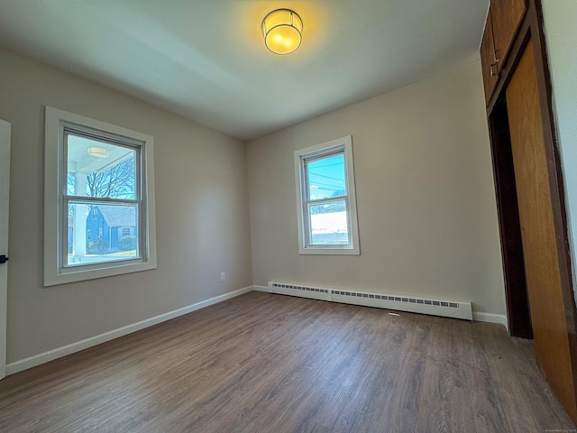 unfurnished room with dark wood-type flooring, baseboards, a healthy amount of sunlight, and baseboard heating