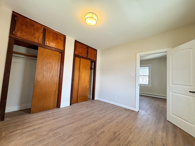 unfurnished bedroom with baseboard heating, baseboards, two closets, and wood finished floors