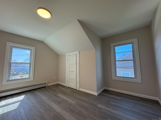 additional living space with baseboards, a wealth of natural light, baseboard heating, and dark wood-style flooring