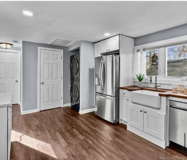 kitchen featuring a sink, white cabinetry, stacked washer and dryer, appliances with stainless steel finishes, and butcher block counters