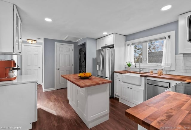 kitchen with a sink, stacked washer and dryer, white cabinets, appliances with stainless steel finishes, and butcher block counters
