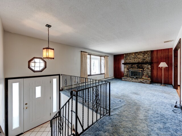 carpeted foyer with visible vents, a notable chandelier, a stone fireplace, a textured ceiling, and wooden walls
