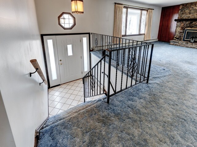 carpeted entrance foyer with a stone fireplace and stairway