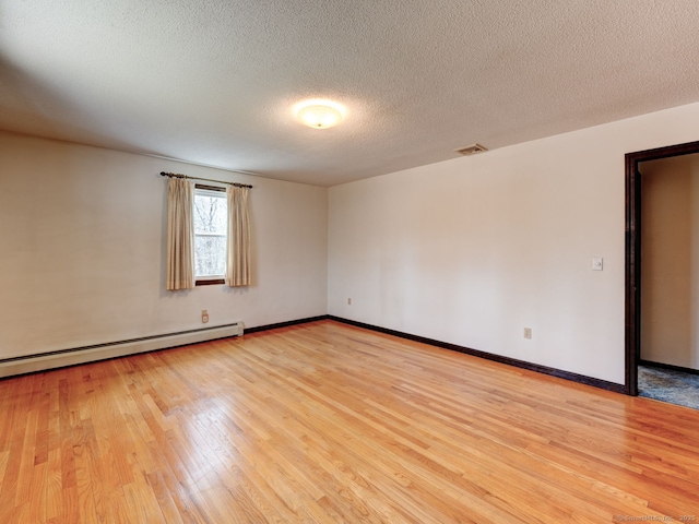 empty room with a baseboard heating unit, baseboards, a textured ceiling, visible vents, and light wood finished floors