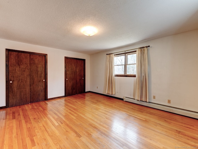 unfurnished bedroom featuring light wood-style flooring, a baseboard radiator, two closets, and a textured ceiling