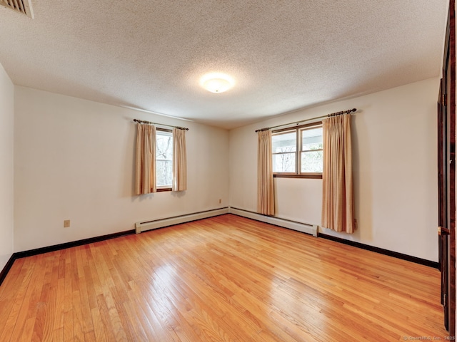 empty room with light wood-style flooring, a textured ceiling, visible vents, baseboard heating, and baseboards