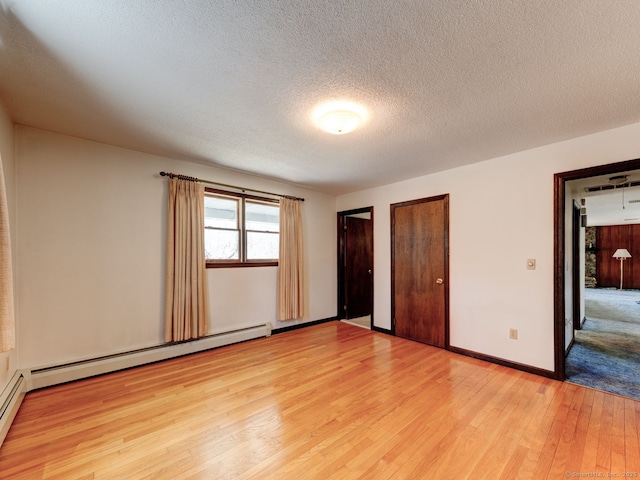 unfurnished bedroom featuring light wood-style flooring, a textured ceiling, baseboard heating, multiple closets, and baseboards