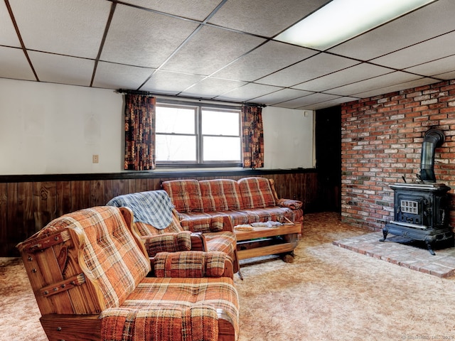 carpeted living room featuring wooden walls, a wood stove, a paneled ceiling, and wainscoting