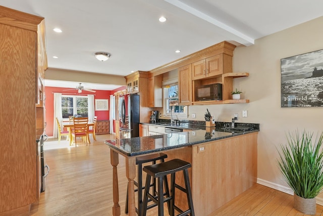kitchen featuring a peninsula, a kitchen breakfast bar, dark stone countertops, light wood-type flooring, and black appliances